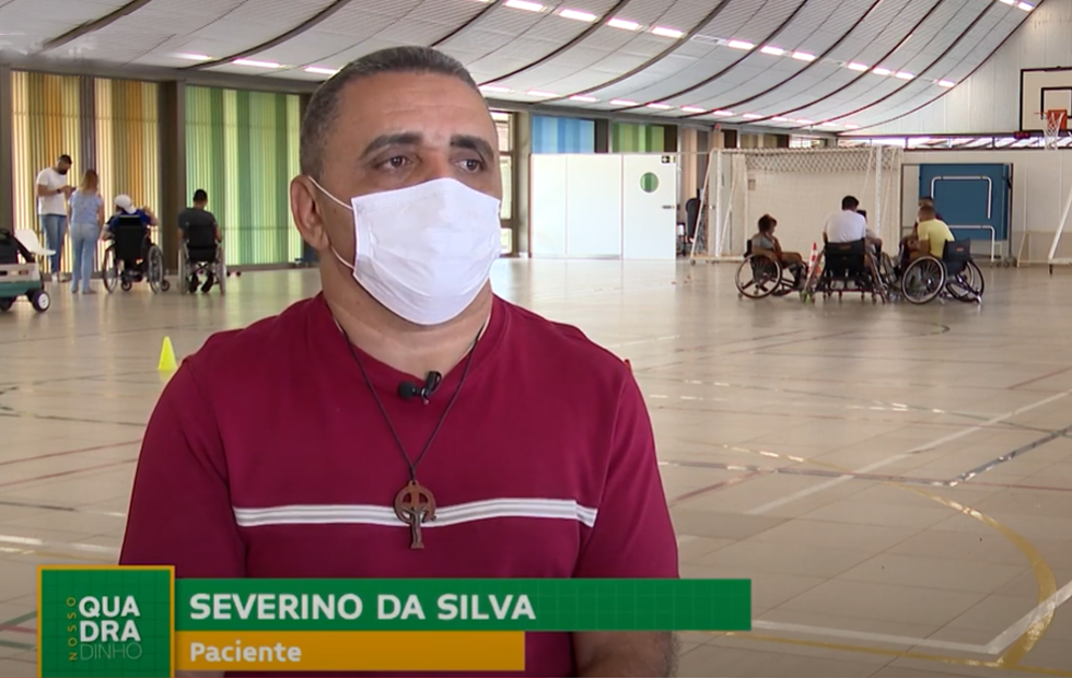 Severino da Silva, paciente do SARAH Brasília em entrevista à TV Câmara Distrital De camisa vermelha, o paciente e jogador de rugy em cadeira de rodas Severino da Silva fala sobre sua reabilitação. Ao fundo, na quadra poliesportiva do Hospital SARAH Lago Norte, outros cadeirantes conversam em grupos.