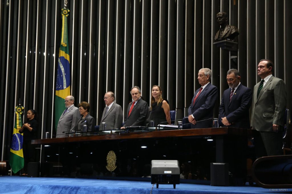 Dra. Lúcia Willadino Braga em pé junto as outras autoridades durante a execução do hino nacional Dra. Lúcia Willadino Braga em pé junto as outras autoridades durante a execução do hino nacional
