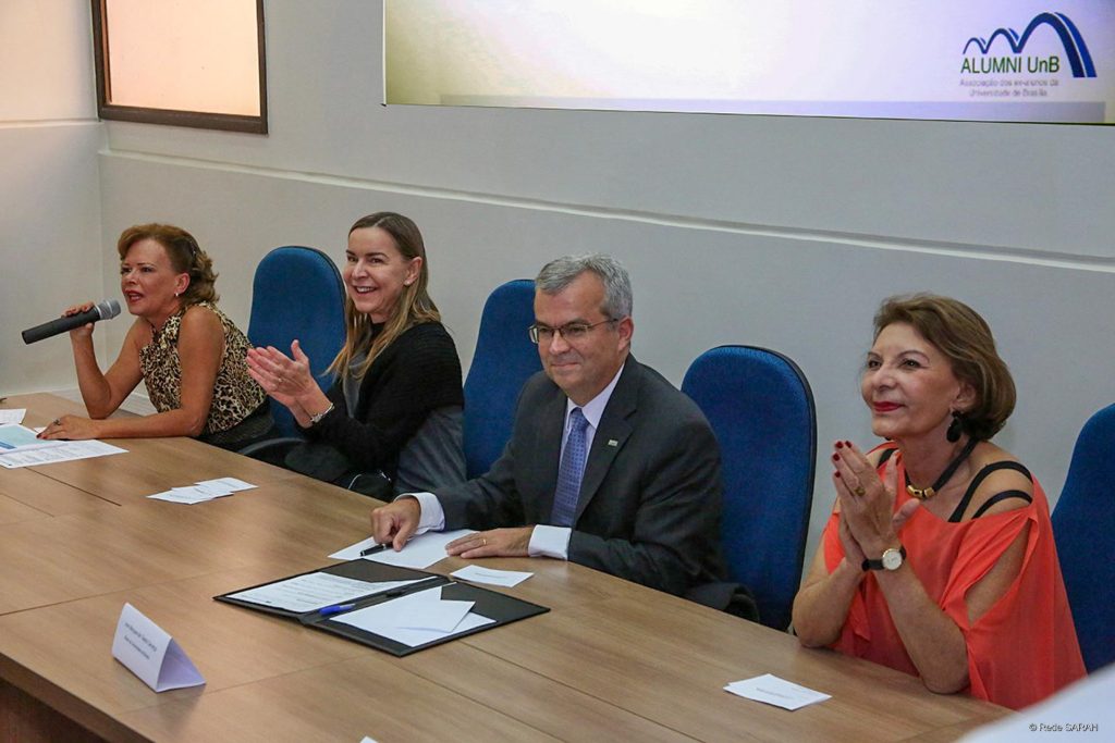 Dra. Lúcia Willadino Braga participando da reunião especial, em sua homenagem, da Alumni UnB Imagem de reunião especial da Alumni UnB – Associação dos Ex-alunos da Universidade de Brasília, mostra homens e mulheres sentados à uma mesa e frente a um auditório.