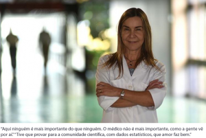 20151101 A Saúde Só Muda Se A Educação Mudar 01 De pé, vestindo jaleco branco e de braços cruzados, Lúcia Willadino Braga posa para foto em local não identificado, com o fundo da imagem desfocado.