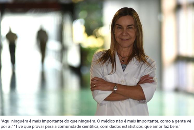 20151101 A Saúde Só Muda Se A Educação Mudar 01 De pé, vestindo jaleco branco e de braços cruzados, Lúcia Willadino Braga posa para foto em local não identificado, com o fundo da imagem desfocado.