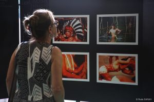 Convidada acompanhando a exposição De pé, mulher examina fotografias de indígenas brasileiros, coladas em um mural, como parte de exposição fotográfica no SARAH Brasília.