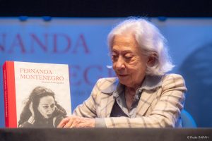 Fernanda Montenegro com seu livro “Itinerário Fotobiográfico” Sentada a uma mesa, no palco do Teatro SARAH Brasília, Fernanda Montenegro segura uma cópia do seu livro "Itinerário Fotobiográfico".