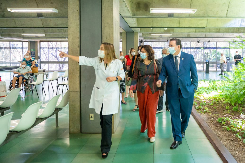 Dra. Lúcia Willadino Braga mostrando o SARAH Brasília à ministra da Saúde, Nísia Trindade Vestindo jaleco branco, Dra. Lúcia Willadino Braga apresenta o ambulatório do SARAH Brasília Centro à ministra da Saúde, Nísia Trindade, vestindo blusa de manga comprida em tons de vermelho e azul com calças vermelhas, e ao secretário-executivo da Saúde, Swedenberger Barbosa, vestindo terno azul e gravata. Ao fundo, membros da comitiva ministerial e da equipe do hospital acompanham a visita.