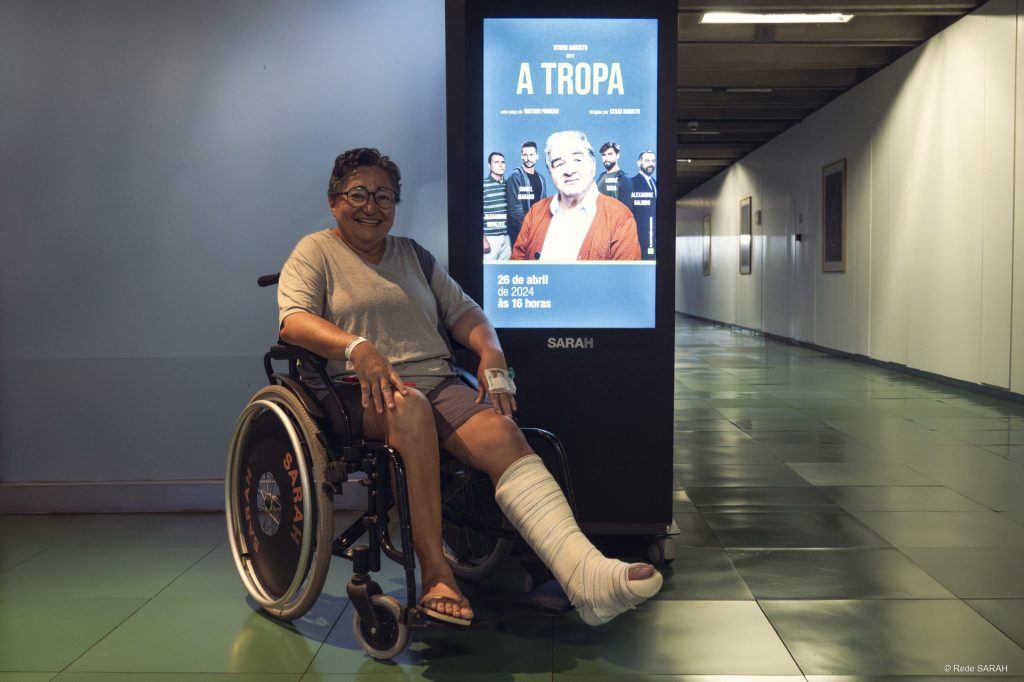 Paciente Maria de Jesus ao lado do cartaz da peça