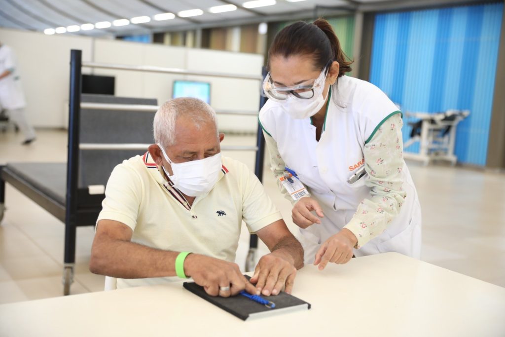 Paciente do SARAH sendo auxiliado por uma enfermeira da Rede em uma atividade de reabilitação